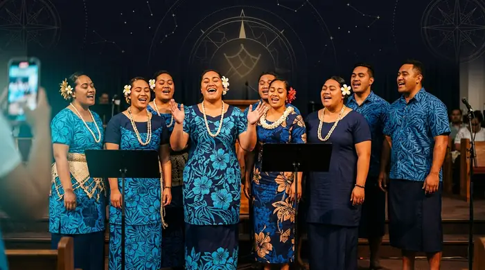 A Pacific Islander church choir singing together, one member recording the moment on a phone
